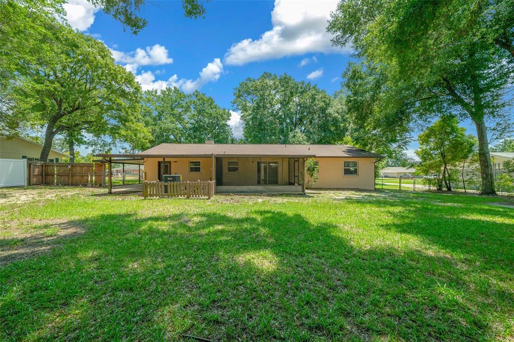 The exterior rear view of a single-story house features a screened porch and large yard — 1820 SE 57TH AVENUE, OCALA, FL