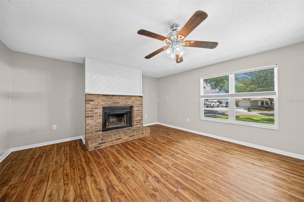 A living room features wood-look flooring, a brick fireplace, and a ceiling fan — 1820 SE 57TH AVENUE, OCALA, FL