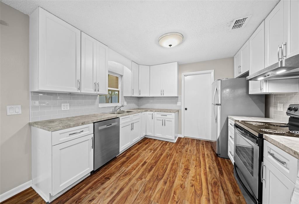 A kitchen with white cabinets, stainless steel appliances, gray countertops, and wood-look flooring — 1820 SE 57TH AVENUE, OCALA, FL