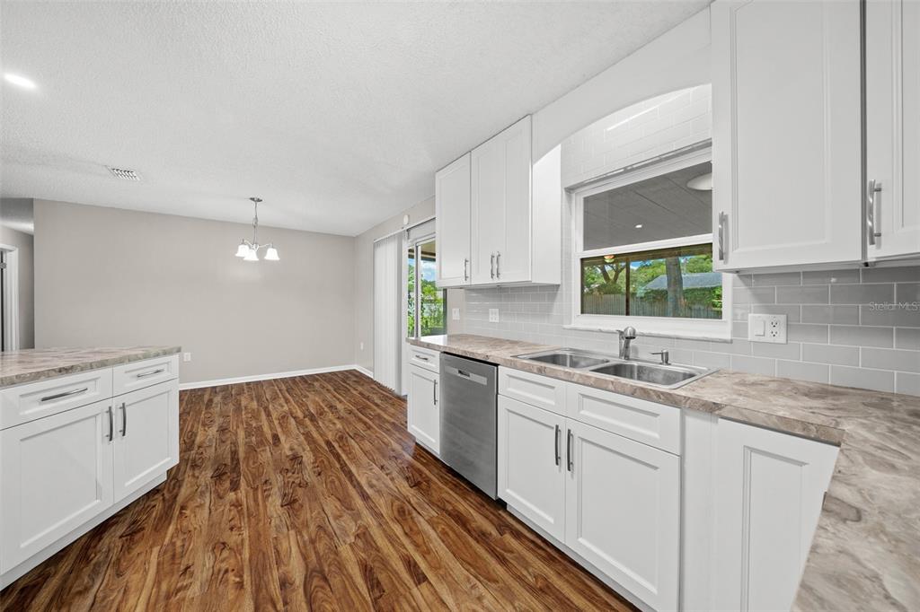 A kitchen with white cabinets, gray subway tile backsplash, and wood-look flooring — 1820 SE 57TH AVENUE, OCALA, FL