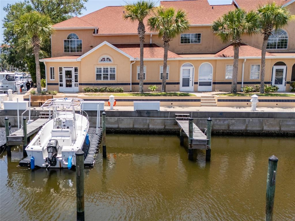 A white motorboat is docked at a concrete bulkhead in front of a tan building — 49B MARINA POINT PLACE UNIT SLIP  49B, PALM COAST, FL