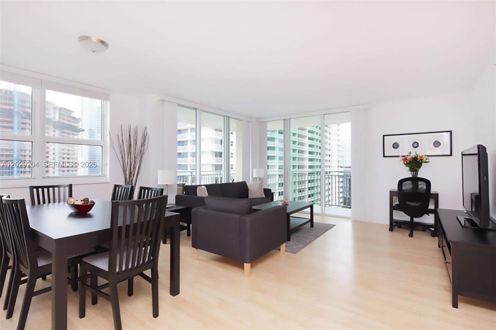A bright living and dining area features dark furniture, light wood floors, and floor-to-ceiling windows — 1155 Brickell Bay Dr # 2701, Miami FL 33131, MIAMI, FL