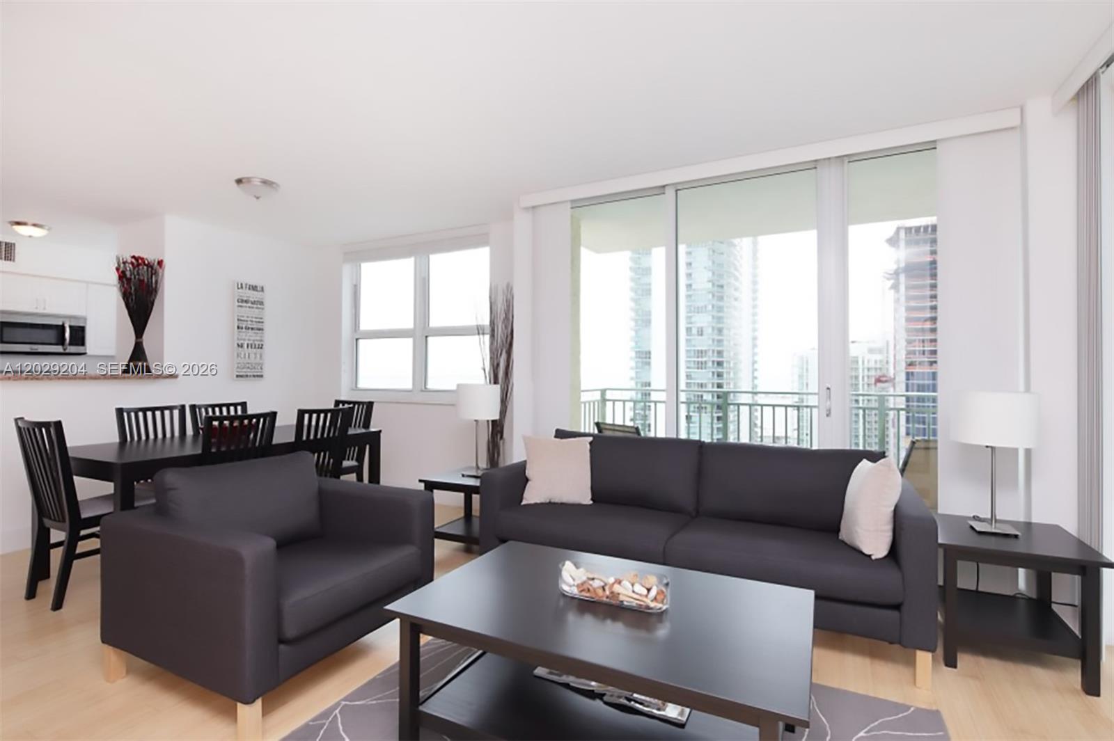 A living and dining room features dark furniture, light wood floors, and a balcony view — 1155 Brickell Bay Dr # 2701, Miami FL 33131, MIAMI, FL