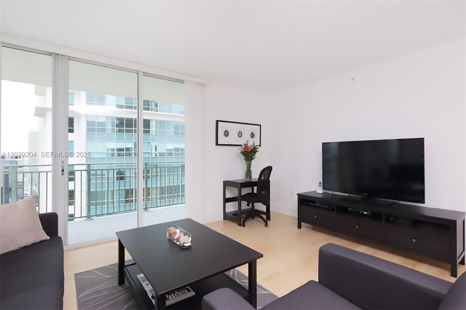 A living room features light wood floors, a dark entertainment console, and a glass balcony door — 1155 Brickell Bay Dr # 2701, Miami FL 33131, MIAMI, FL