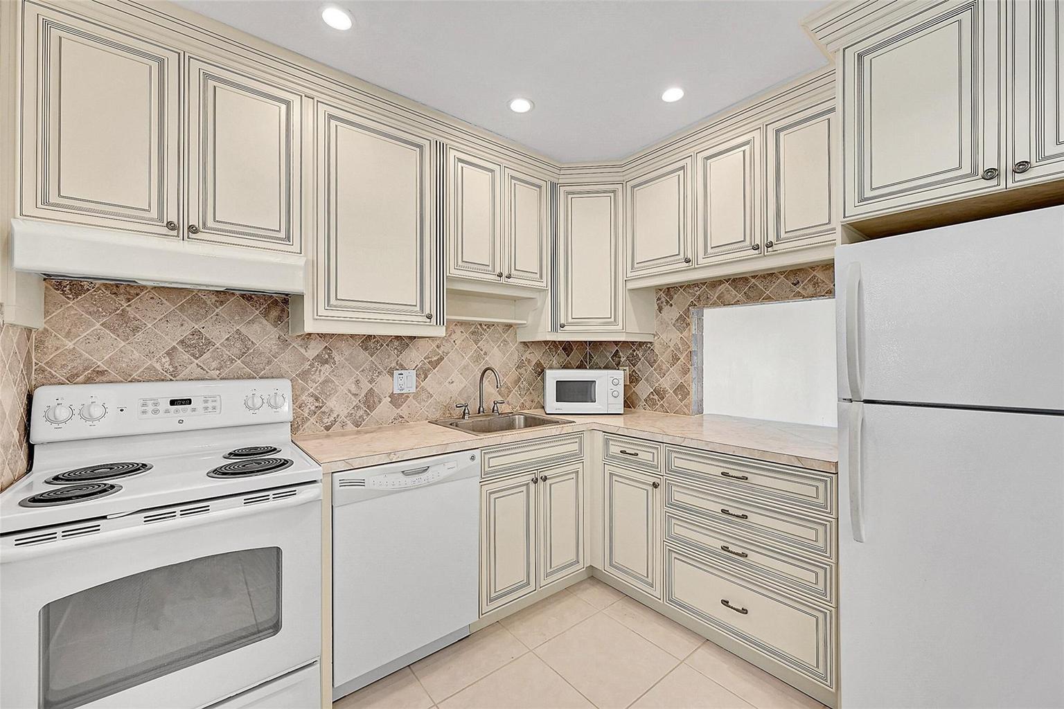 A kitchen features off-white cabinets with dark trim, a white stove, and a tiled backsplash — 23 Abbey Lane # 202, Delray Beach FL 33446, DELRAY BEACH, FL