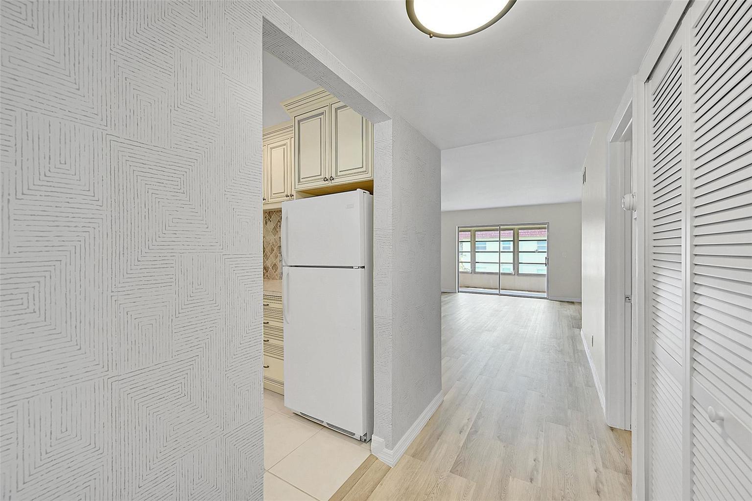A hallway leads past a kitchen with a white refrigerator toward a bright living area — 23 Abbey Lane # 202, Delray Beach FL 33446, DELRAY BEACH, FL