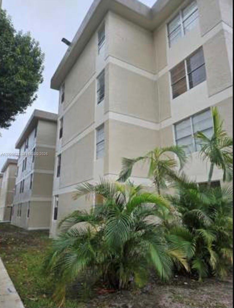 A low-angle exterior view of a multi-story beige apartment building with palm trees — 1805 W 56th St # 209, Hialeah FL 33012, HIALEAH, FL