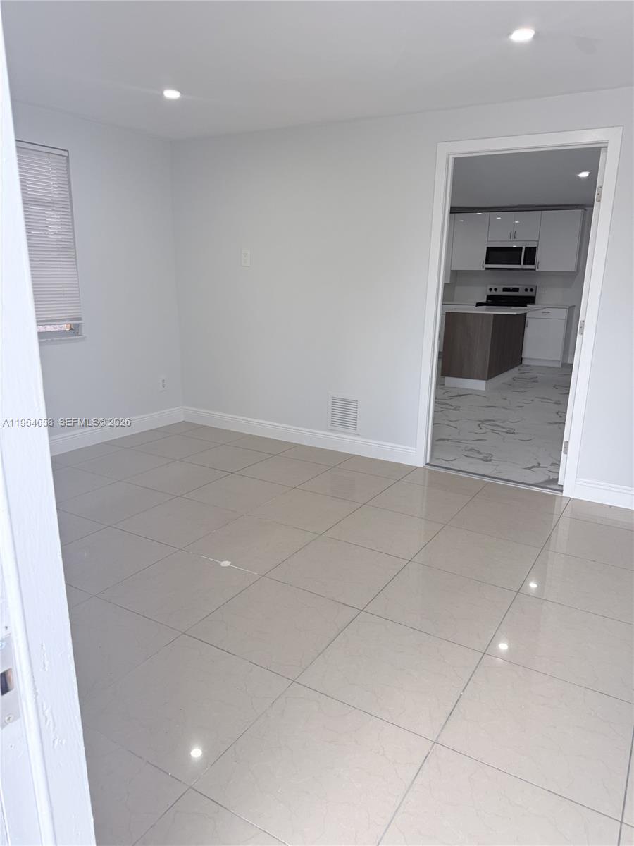 A room with light-colored tile flooring and a doorway leading to a modern kitchen — 6829 SW 25th St, Miami FL 33155, MIAMI, FL
