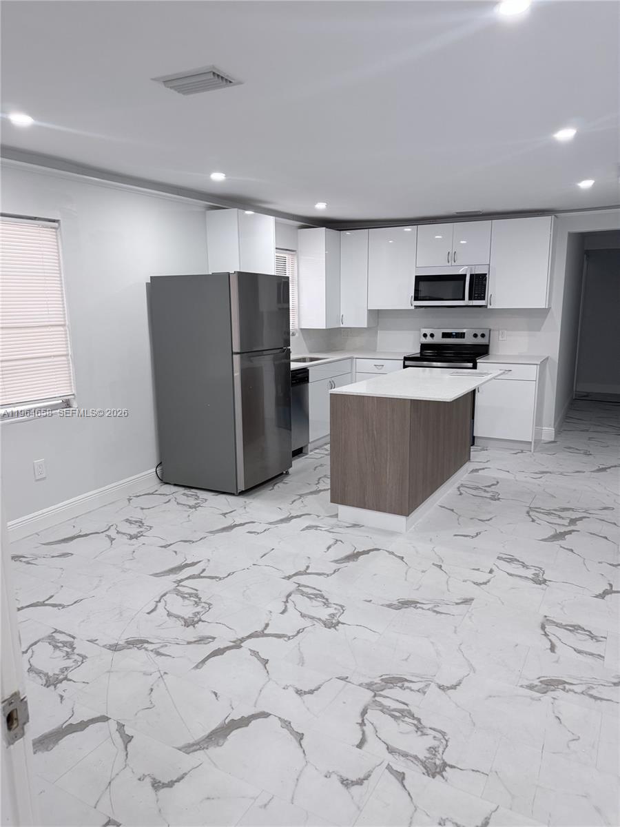 A kitchen features white cabinets, a gray refrigerator, a wood-toned island, and marble-patterned tile flooring — 6829 SW 25th St, Miami FL 33155, MIAMI, FL