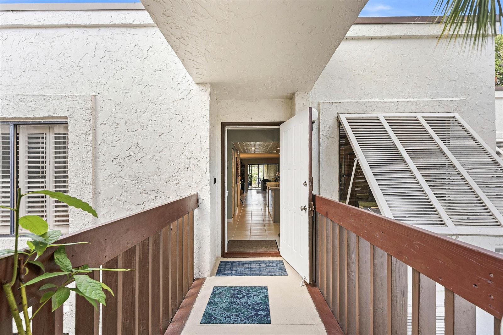 An exterior walkway leads to an open white front door revealing a tiled interior hallway — 10155 Mangrove Drive # 204, Boynton Beach FL 33437, BOYNTON BEACH, FL