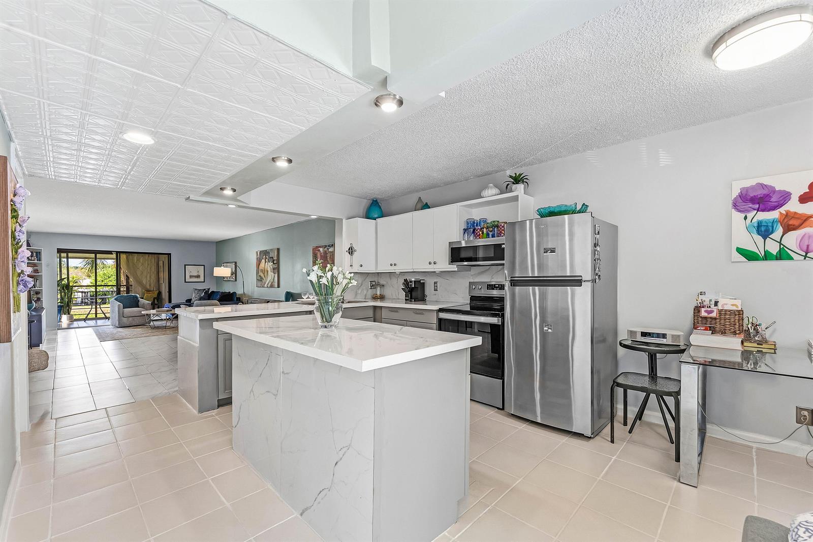 A kitchen with white cabinets, a marble-topped island, and stainless steel appliances opens to a living area — 10155 Mangrove Drive # 204, Boynton Beach FL 33437, BOYNTON BEACH, FL