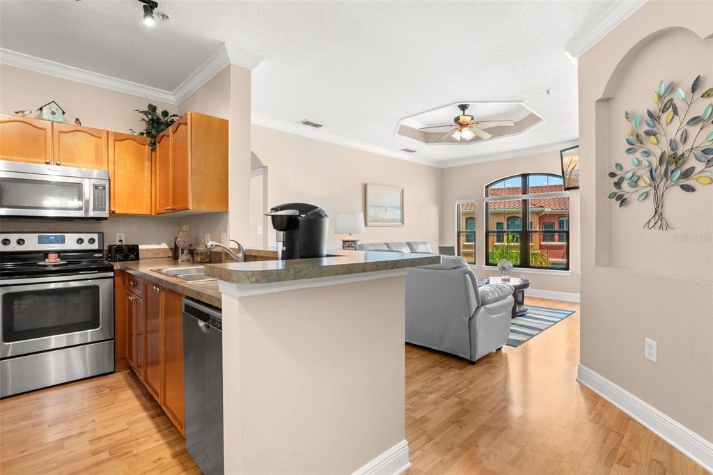 A kitchen with wood cabinets and stainless appliances opens into a living room with hardwood floors — 2765 VIA CIPRIANI UNIT 1232A, CLEARWATER, FL