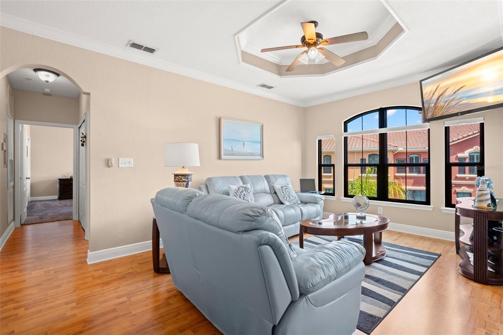 A living room features light blue leather furniture, hardwood floors, and a tray ceiling — 2765 VIA CIPRIANI UNIT 1232A, CLEARWATER, FL