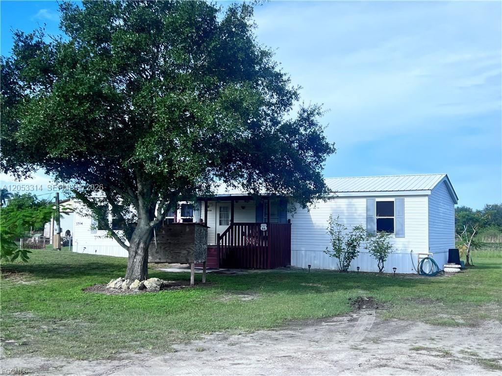 A white manufactured home with a metal roof and a wooden deck stands under a tree — 3704 Dustin, La Belle FL 33935, LA BELLE, FL