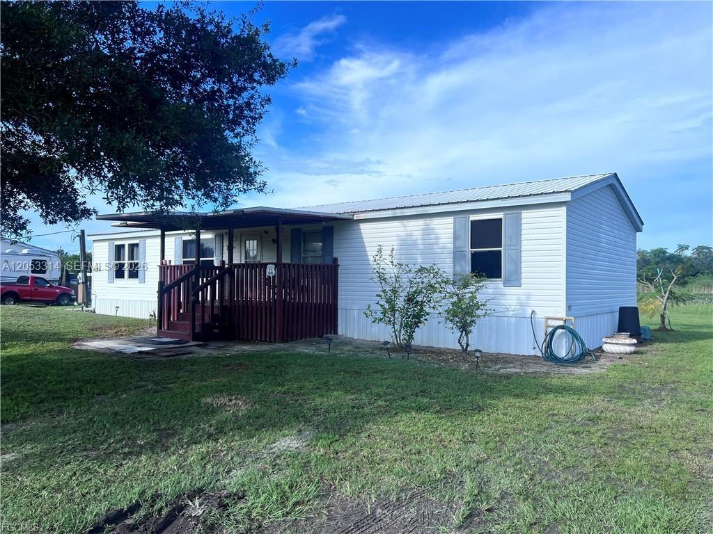 A white mobile home features a wooden porch and a metal roof under a blue sky — 3704 Dustin, La Belle FL 33935, LA BELLE, FL