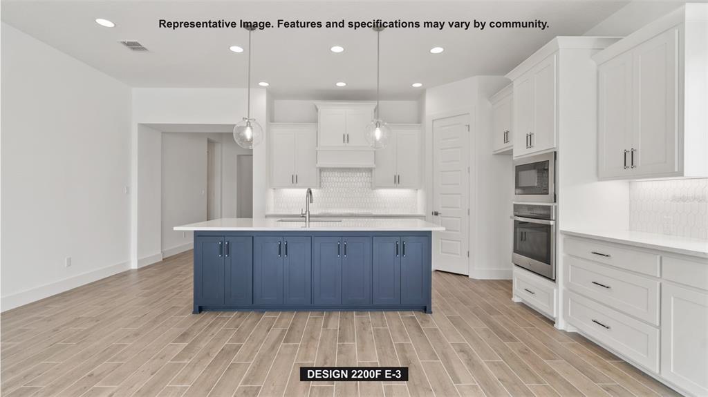 This kitchen features white cabinets, a blue island, stainless steel appliances, and wood-look tile flooring — 7910 BON AIR WAY, PARRISH, FL