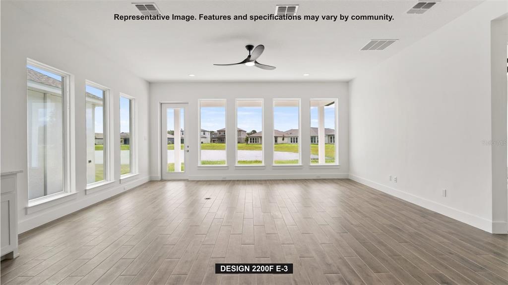 This bright, open-concept living room features wood-look tile flooring, a ceiling fan, and large windows — 7910 BON AIR WAY, PARRISH, FL