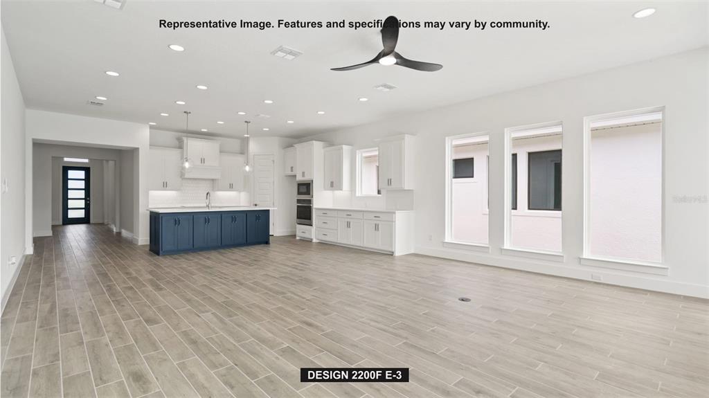 This open-concept kitchen and living area features white cabinetry, a blue island, and wood-look flooring — 7910 BON AIR WAY, PARRISH, FL