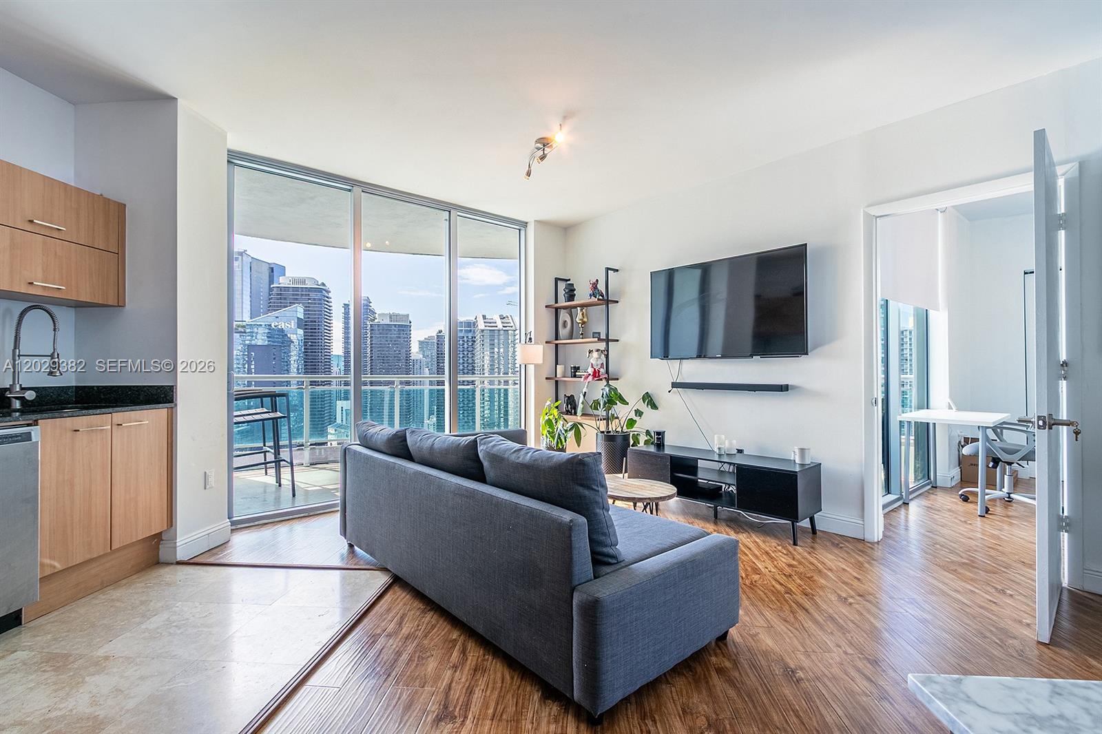 A living room with wood flooring, a grey sofa, a wall-mounted television, and floor-to-ceiling windows — 350 S Miami Ave # 3914, Miami FL 33130, MIAMI, FL