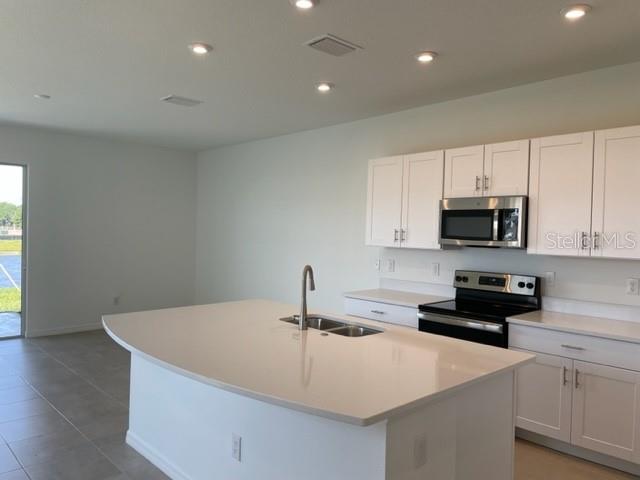 A modern kitchen features white cabinets, a large island with a sink, and stainless appliances — 5764 HAVEN TERRACE, NOKOMIS, FL