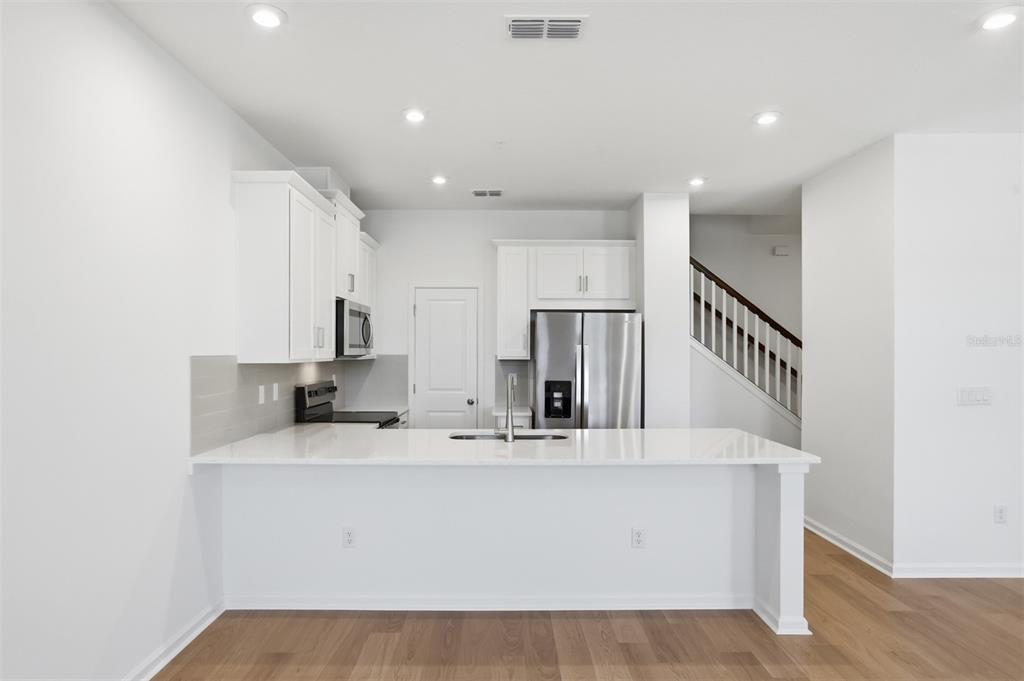 A modern kitchen features white cabinets, stainless steel appliances, and a white quartz breakfast bar — 10063 GAZEBO ALLEY, ORLANDO, FL