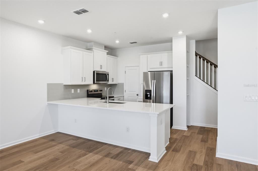 A modern kitchen features white cabinets, stainless steel appliances, and a white quartz island countertop — 10063 GAZEBO ALLEY, ORLANDO, FL