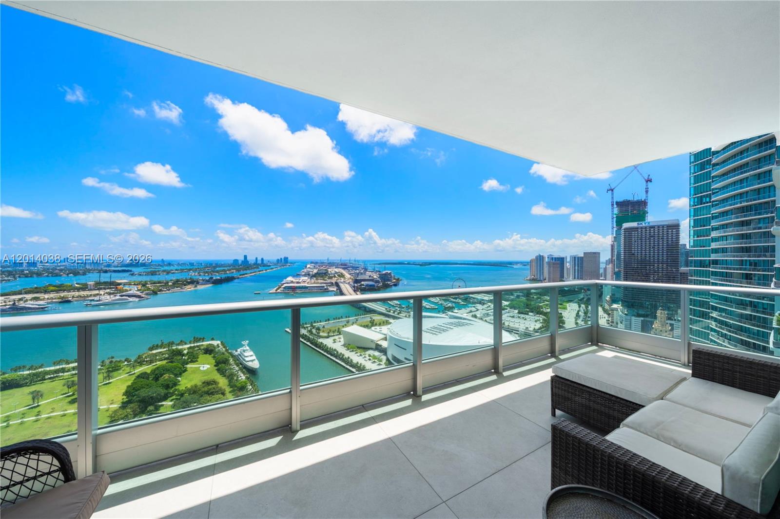 A high-rise balcony features outdoor furniture overlooking a bay, a park, and a city skyline — 900 Biscayne Blvd # 4202, Miami FL 33132, MIAMI, FL