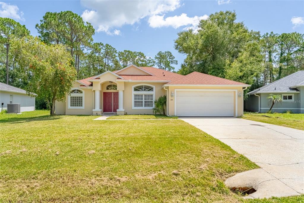 A single-story house with a red roof, beige stucco exterior, and a two-car garage — 103 WOODSIDE DRIVE, PALM COAST, FL