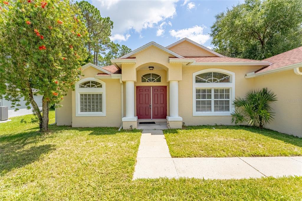 A single-story house with a beige stucco exterior, red double doors, and a concrete walkway — 103 WOODSIDE DRIVE, PALM COAST, FL