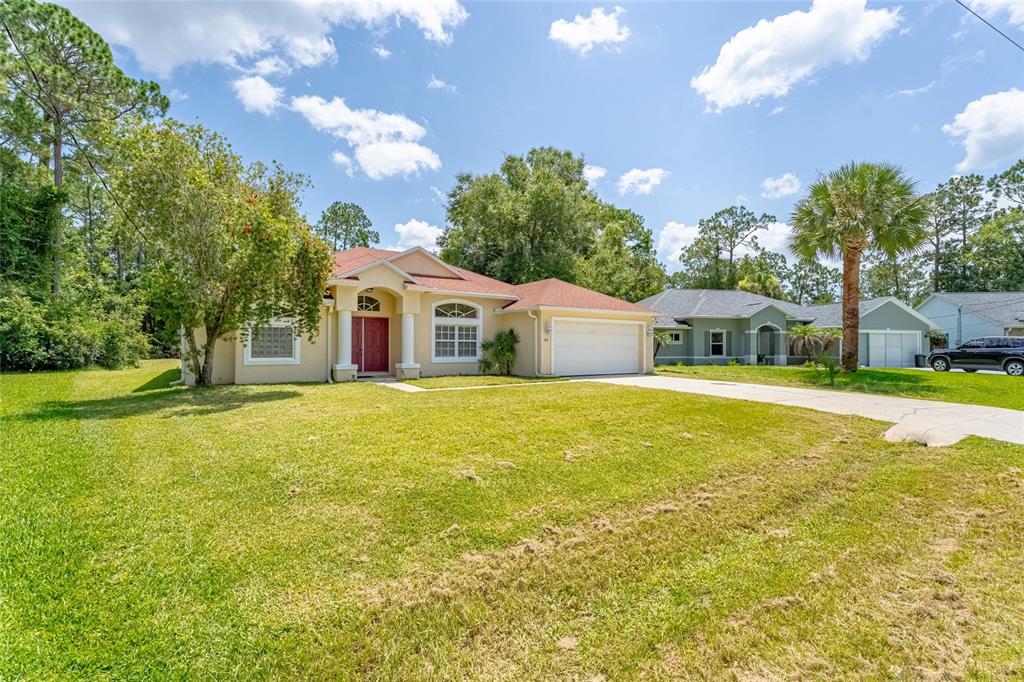 A single-story suburban house with a red front door, two-car garage, and a grassy lawn — 103 WOODSIDE DRIVE, PALM COAST, FL