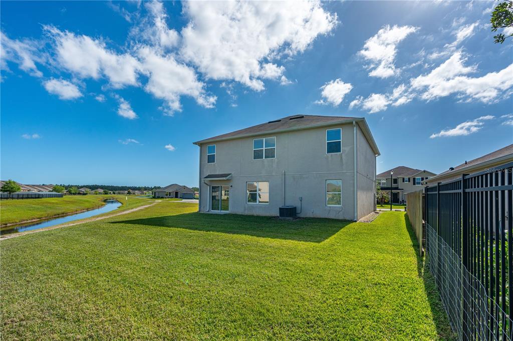 The rear exterior of a two-story house features a grassy yard, a canal, and fencing — 5324 ROYAL PLANTATION BOULEVARD, PORT ORANGE, FL
