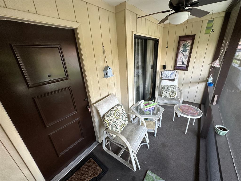A covered patio features a brown door, two white chairs, two small tables, and a ceiling fan — 3500 EL CONQUISTADOR PARKWAY UNIT 314, BRADENTON, FL