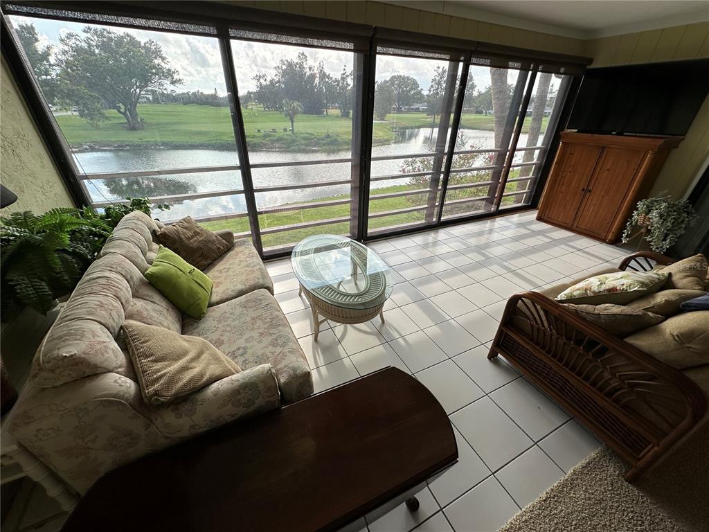 A sunroom with tile flooring, a sofa, a coffee table, and large windows overlooking a pond — 3500 EL CONQUISTADOR PARKWAY UNIT 314, BRADENTON, FL
