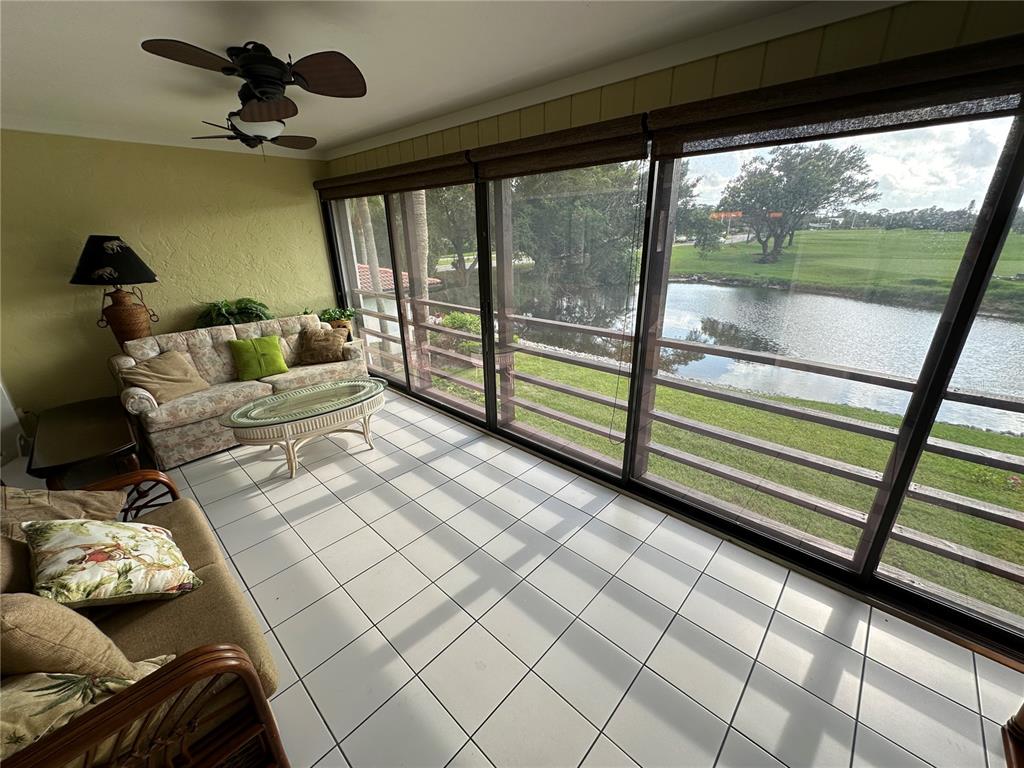 A sunroom features tile flooring, two sofas, and large windows overlooking a pond and golf course — 3500 EL CONQUISTADOR PARKWAY UNIT 314, BRADENTON, FL
