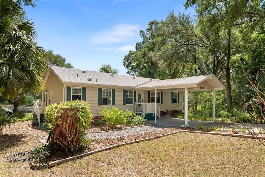 A single-story house with beige siding, green shutters, and an attached carport sits outdoors — 5841 SE 164TH AVENUE, OCKLAWAHA, FL