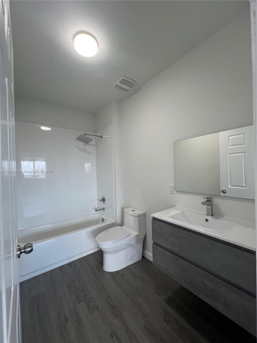 A modern bathroom features a white bathtub, a toilet, and a gray vanity with mirror — 2311 NW 22nd Ave # 207, Miami FL 33142, MIAMI, FL