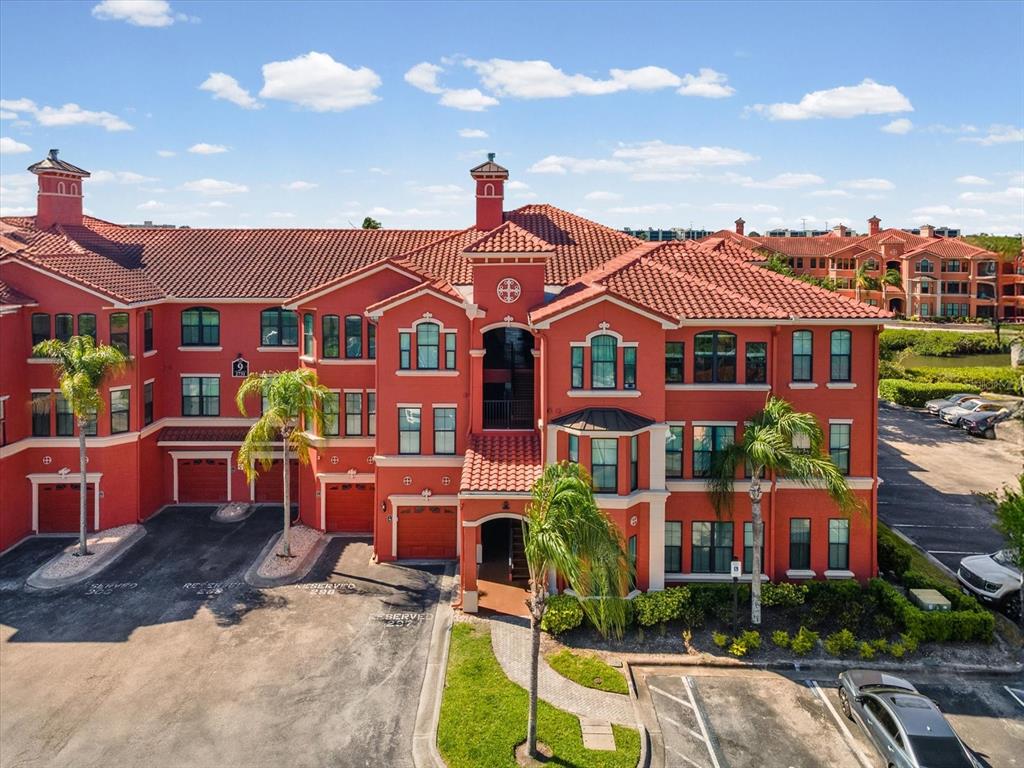 An exterior view of a multi-story red stucco apartment building with a terracotta tile roof — 2731 VIA CAPRI UNIT 925, CLEARWATER, FL