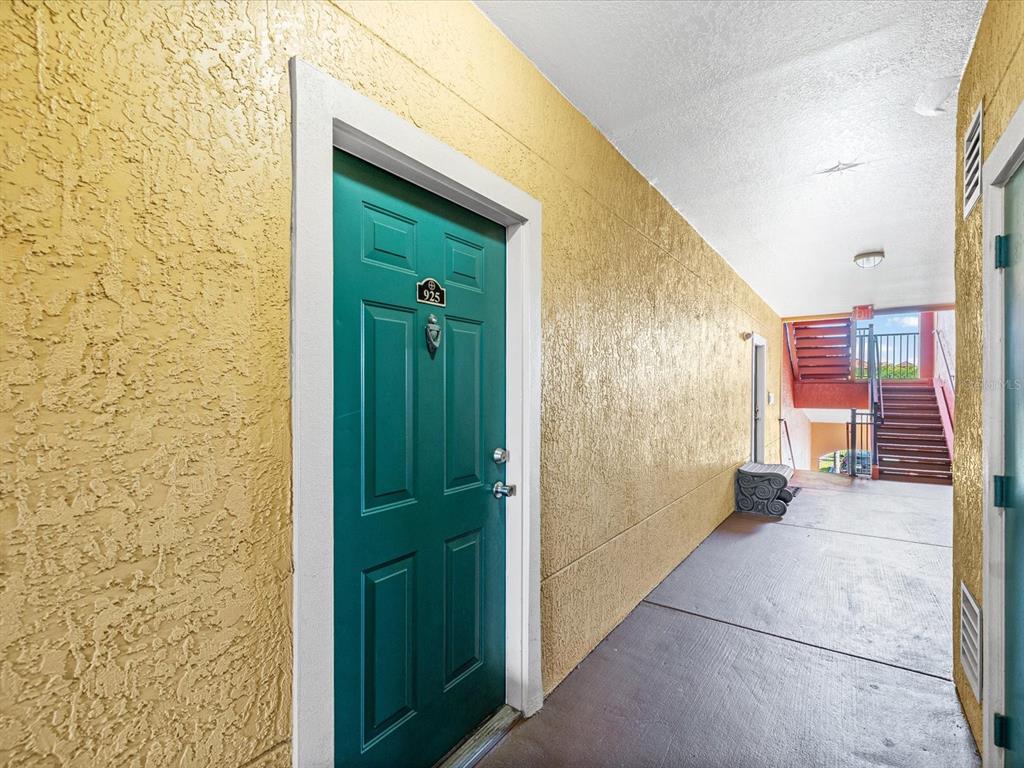 A teal front door with the number 925 sits in a yellow stucco outdoor hallway — 2731 VIA CAPRI UNIT 925, CLEARWATER, FL
