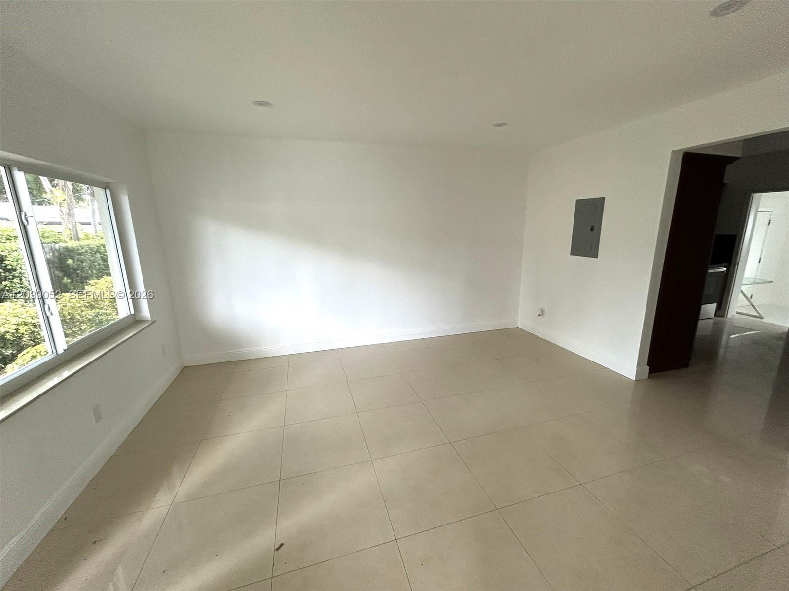 An empty room features white walls, large beige floor tiles, and a single window — 1530 NE 110th Ter, Miami FL 33161, MIAMI, FL