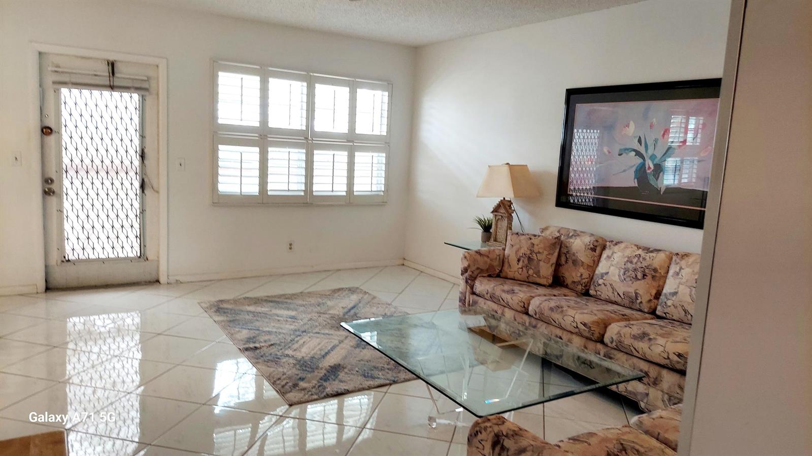 A living room features white tile floors, a floral sofa, and a glass coffee table — 4079 Cornwall D # 4079, Boca Raton FL 33434, BOCA RATON, FL