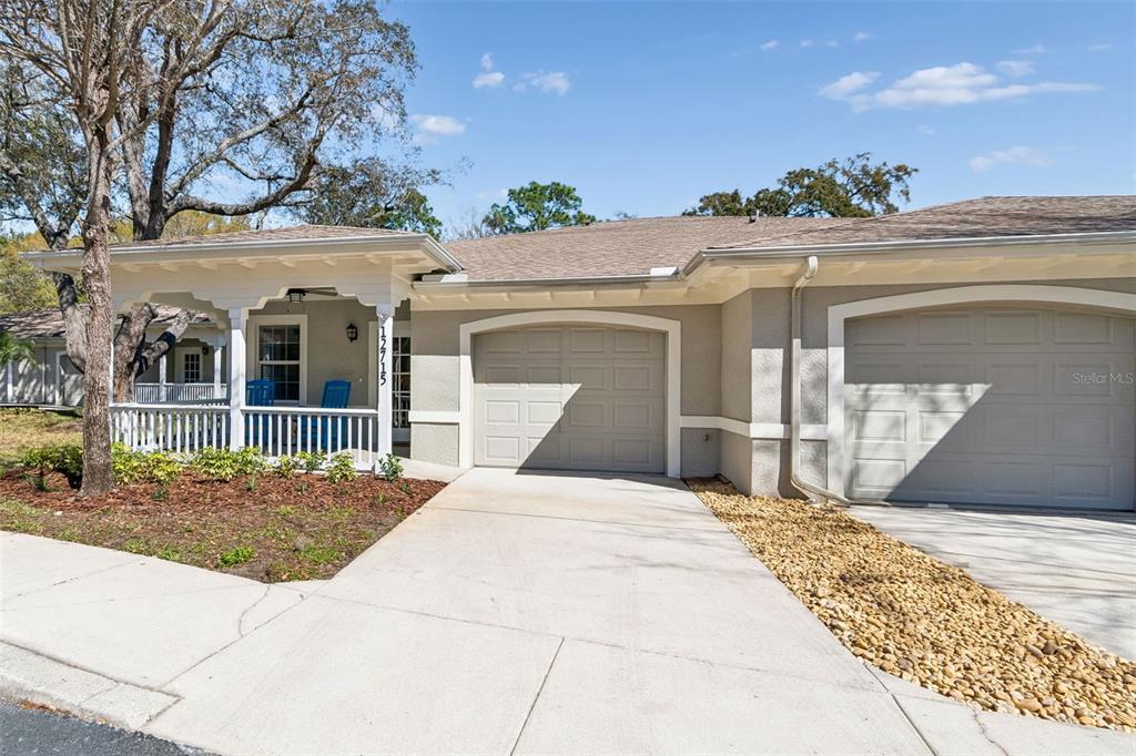 A single-story house exterior features a covered front porch, two garage doors, and landscaping — 12715 TAYLOR NICOLAS DRIVE, TAMPA, FL