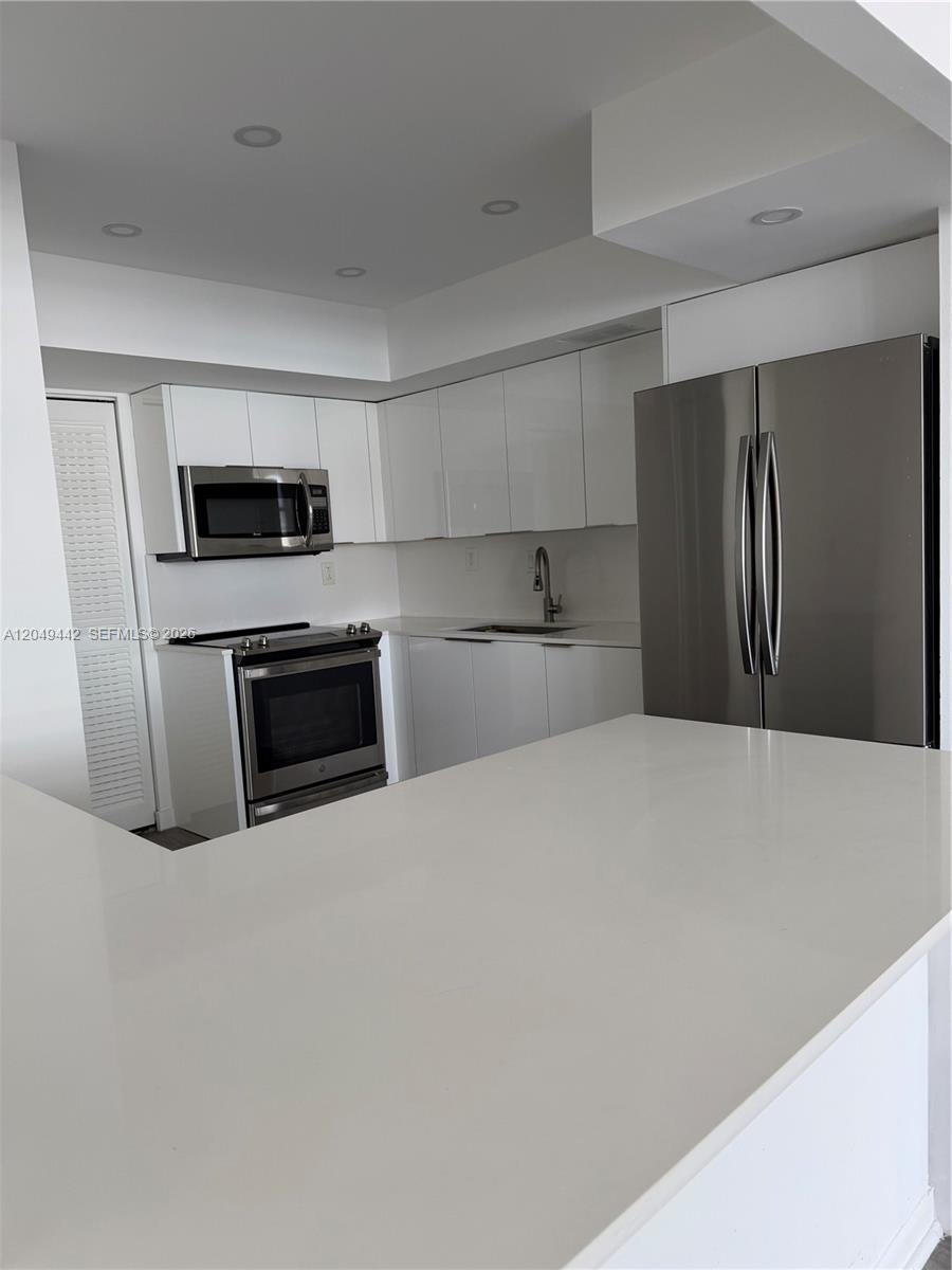 A modern kitchen features white cabinets, stainless steel appliances, and a white quartz countertop — 1420 Brickell Bay Dr # 1005C, Miami FL 33131, MIAMI, FL