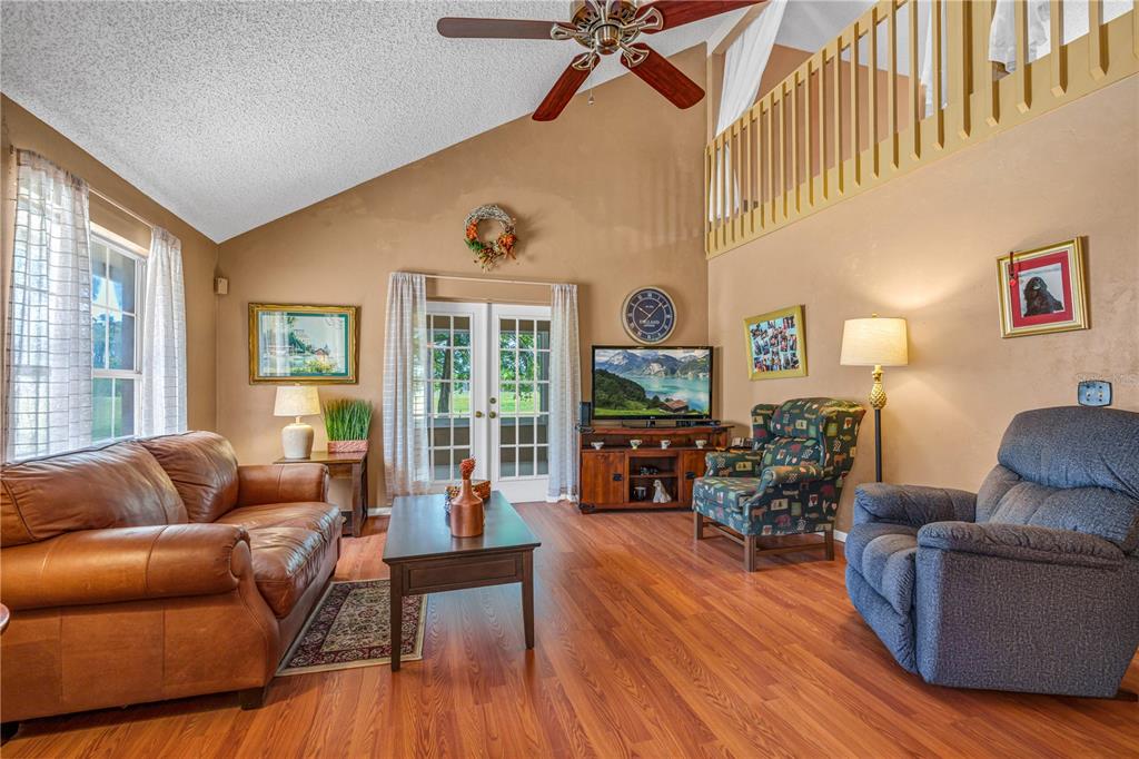 A living room features a vaulted ceiling, wood flooring, a leather sofa, and a loft railing — 524 CROOKED STICK DRIVE, DAYTONA BEACH, FL