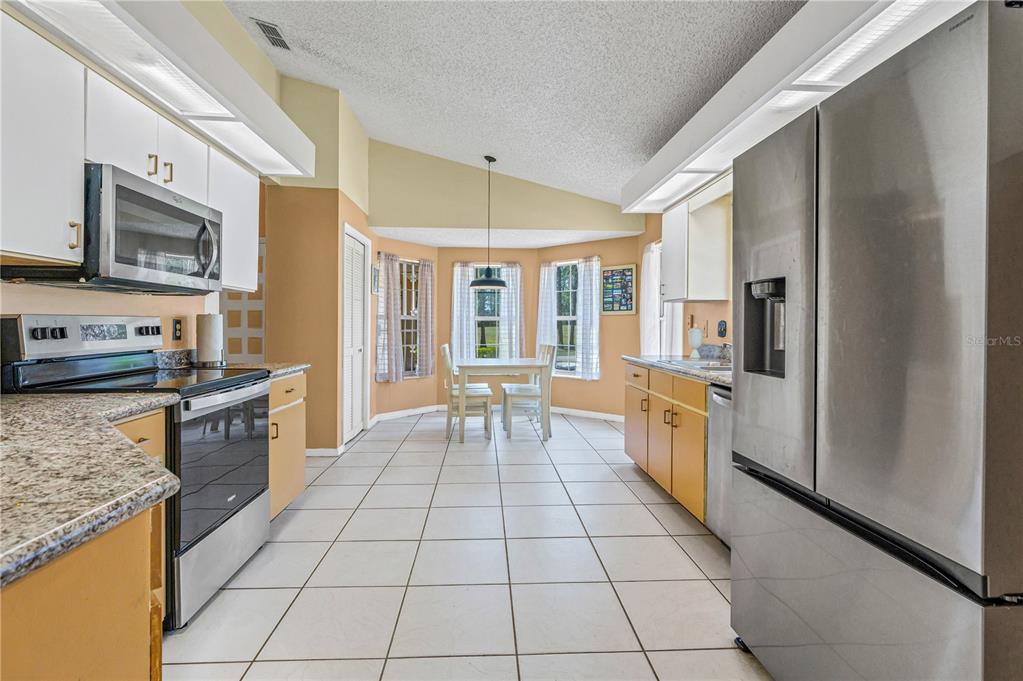 A kitchen with light wood cabinets, granite countertops, stainless steel appliances, and a dining nook — 524 CROOKED STICK DRIVE, DAYTONA BEACH, FL