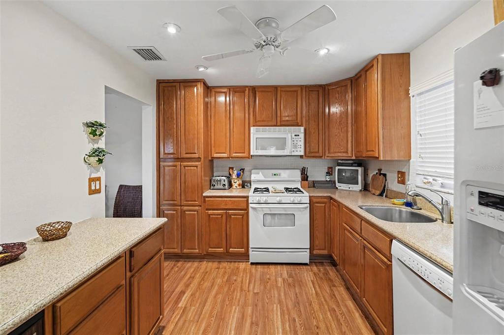 A kitchen features wood cabinets, white appliances, a ceiling fan, and light-colored countertops — 5970 80TH ST N UNIT 301, ST PETERSBURG, FL
