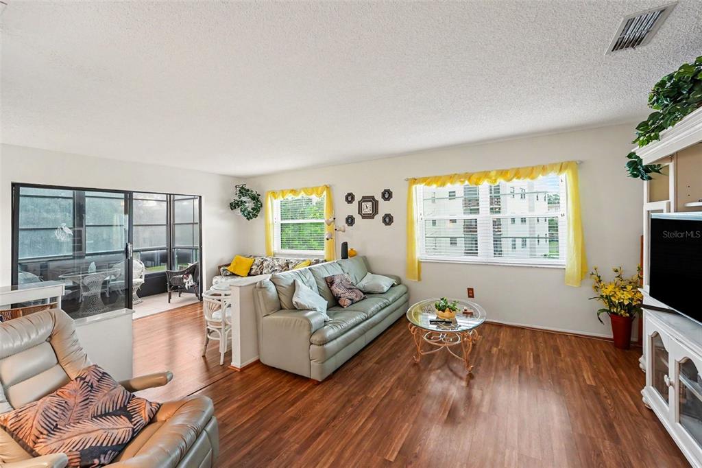 A living room features wood-look flooring, a light-colored sofa, and a glass-topped coffee table — 5970 80TH ST N UNIT 301, ST PETERSBURG, FL