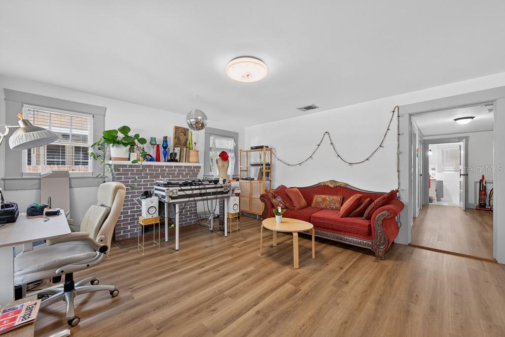 A living room features wood-look flooring, a red sofa, a brick fireplace, and a desk area — 6020 N FLORA VISTA AVENUE, TAMPA, FL