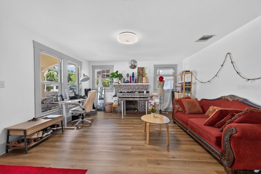 A living room features wood-look flooring, a red sofa, a desk, and a brick fireplace — 6020 N FLORA VISTA AVENUE, TAMPA, FL