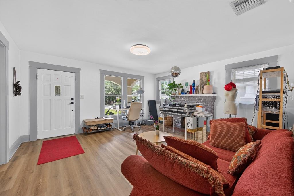 A living room with white walls, gray trim, wood-look flooring, and a red sofa — 6020 N FLORA VISTA AVENUE, TAMPA, FL