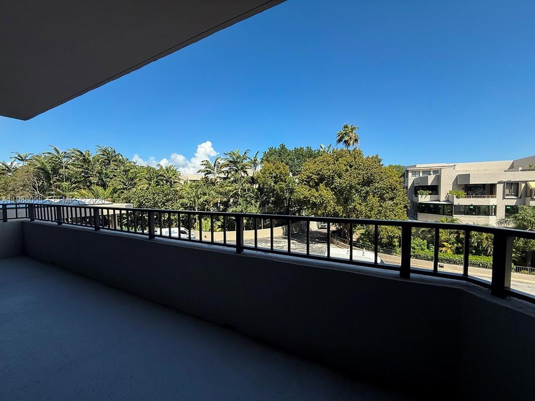 A balcony with a dark metal railing overlooks trees and a neighboring building — 151 Crandon Blvd # 320, Key Biscayne FL 33149, KEY BISCAYNE, FL